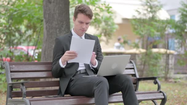 молодий бізнесмен працює над документами та ноутбуком на відкритому повітрі - Кадри, відео