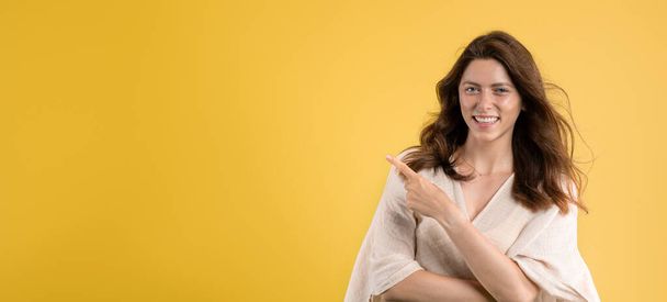 Cheerful young caucasian lady in casual point finger at copy space, isolated on yellow studio background, panorama. Recommendation ad and offer, sale human emotion, fashion - Fotografie, Obrázek