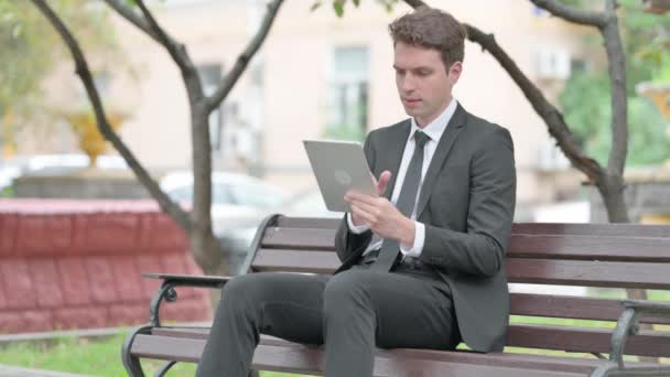 Üzletember ünnepel a táblagépen, miközben ül a padon - Felvétel, videó