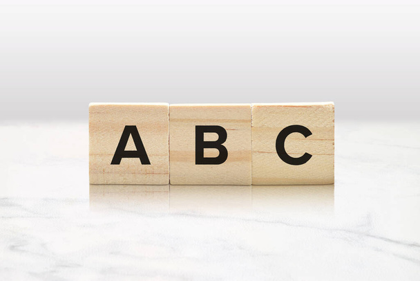 クラシックな白い大理石の背景に対してABCを綴る3つの木製タイル. - 写真・画像