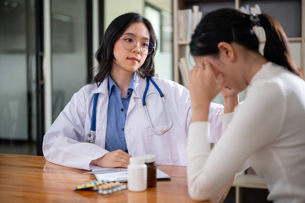 Huolehtiva aasialainen naislääkäri koskettaa stressaantuneen potilaan olkapäätä lohduttaakseen ja rauhoittaakseen häntä puhuessaan sairaalan oireista ja hoitosuunnitelmista.. - Valokuva, kuva