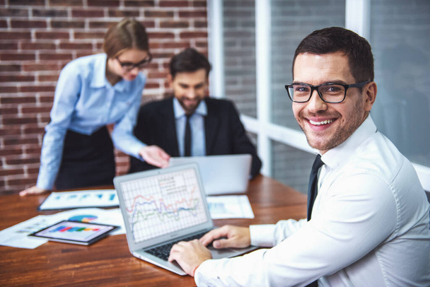 Schöne Geschäftsleute benutzen Laptops, studieren Dokumente, sprechen und lächeln während der Arbeit im Büro - Foto, Bild