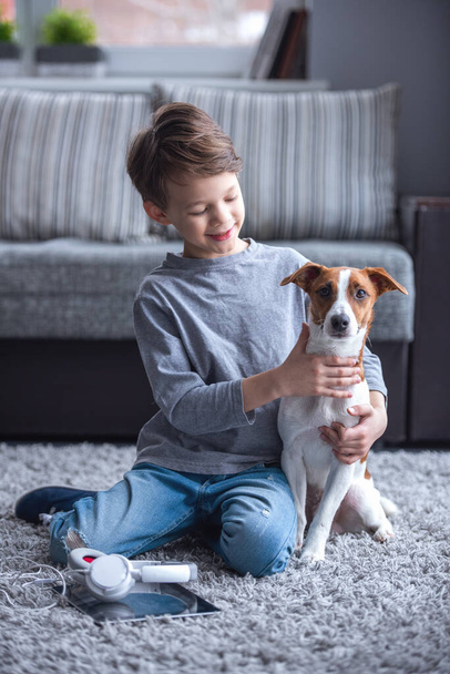 Ragazzino sorride mentre gioca con il suo cane carino a casa
 - Foto, immagini