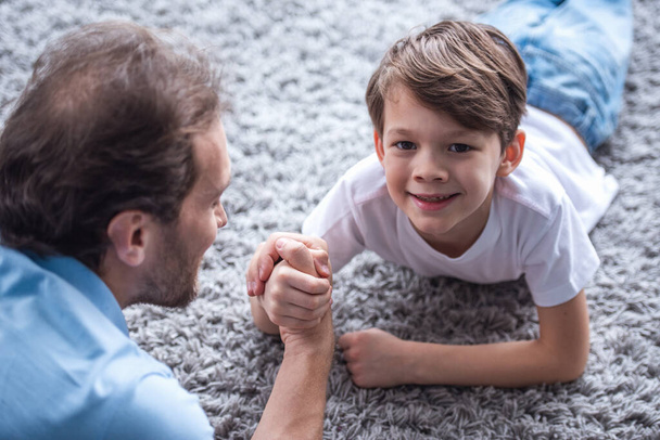 Father and son are wrestling and smiling while spending time together at home - Photo, Image
