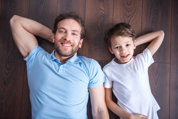 Bovenaanzicht van knappe vader en zijn schattige zoon camera kijken en glimlachen terwijl het besteden van tijd samen thuis - Foto, afbeelding