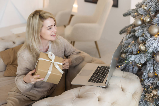 Happy young woman working on laptop in front of christmas tree - Photo, Image