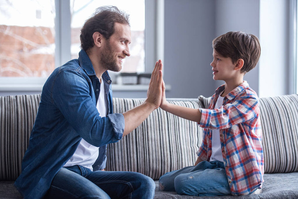 Father and son are giving high five and smiling while spending time together at home - Photo, Image