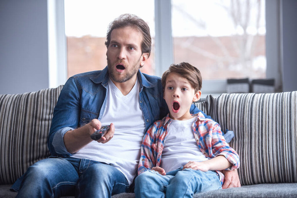 Vader en zoon zijn geschokt Tv kijken terwijl het besteden van tijd samen thuis - Foto, afbeelding