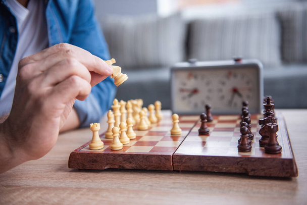 Przycięte zdjęcie młodego mężczyzny trzymającego figurę szachową podczas gry w szachy - Zdjęcie, obraz