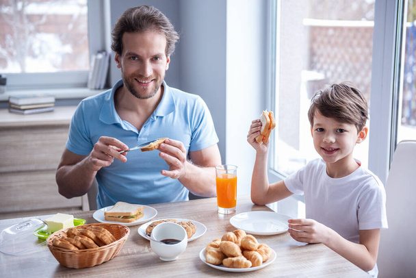 Père et fils regardent la caméra et sourient tout en prenant un petit déjeuner dans la cuisine
 - Photo, image