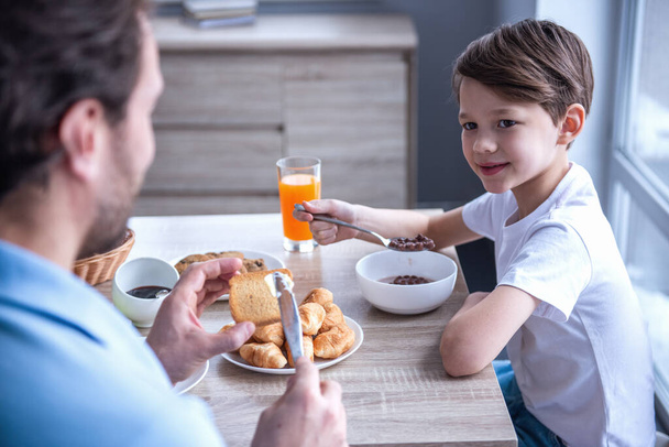 Vater und Sohn reden und lächeln beim Frühstück in der Küche - Foto, Bild