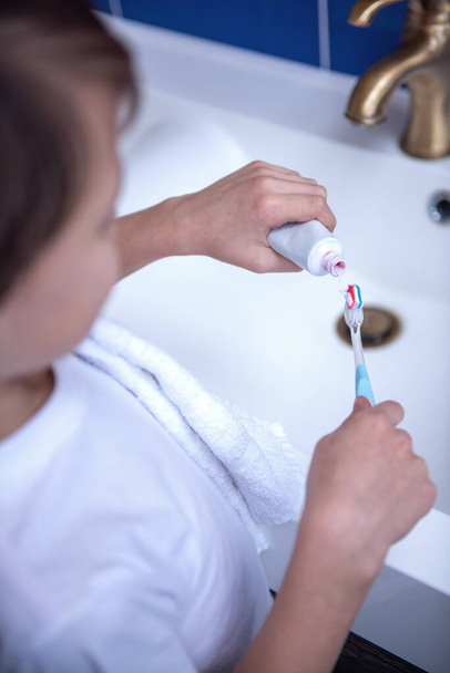 abgeschnittenes Bild eines kleinen Jungen, der beim Zähneputzen im Badezimmer Zahnpasta auf eine Zahnbürste aufträgt - Foto, Bild
