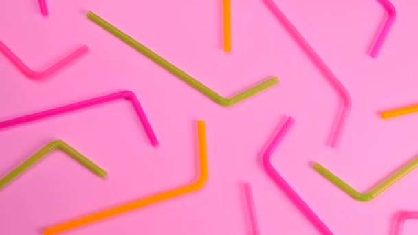 Változatos színű koktélszívószálak forgatása rózsaszín háttéren, felülnézetben, a születésnap, parti vagy évforduló ünneplésének koncepciója. Kiváló minőségű 4k felvételek - Felvétel, videó