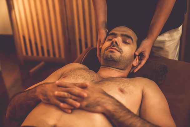 Kaukaski mężczyzna korzystających relaksujący anty-stres masaż głowy i rozpieszczające piękno twarzy rekreacji skóry w ciepłym świetle świec ambient salon spa w luksusowym ośrodku lub hotelu. Cichy zapach - Zdjęcie, obraz