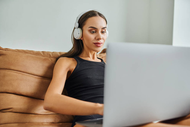 ładna kobieta w słuchawkach bezprzewodowych za pomocą laptopa i siedzi na krześle worek fasoli, zdalnej pracy - Zdjęcie, obraz