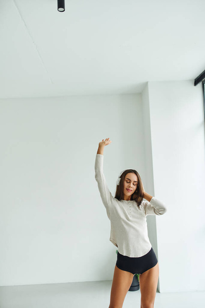 attraente bruna donna a maniche lunghe e mutandine che ballano ascoltando musica in cuffia - Foto, immagini