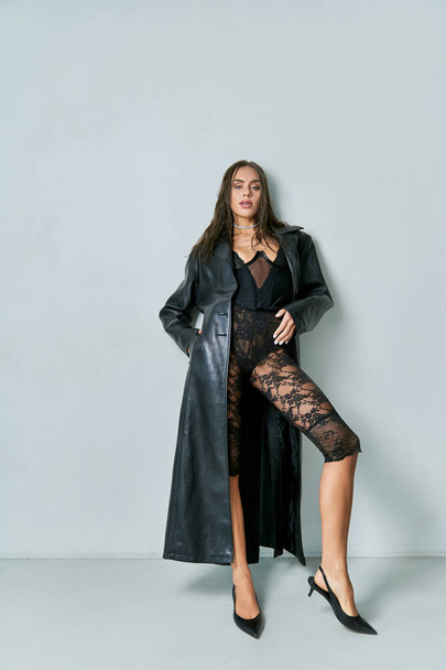 full length of sexy brunette woman in lace underwear and black leather coat posing on grey backdrop - Φωτογραφία, εικόνα