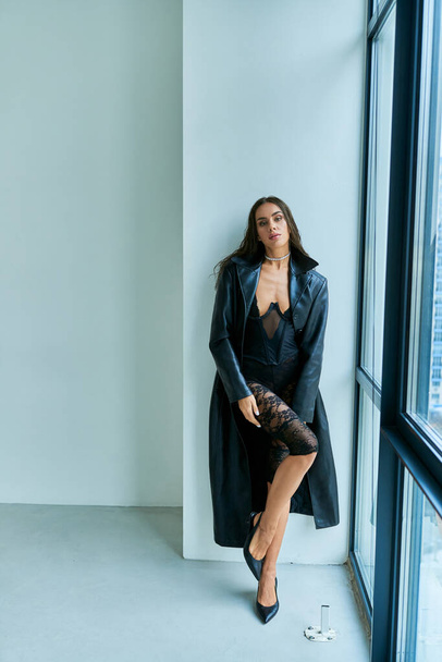passionate woman with brunette wet hair posing in black leather coat and lace underwear near window - Foto, Imagen