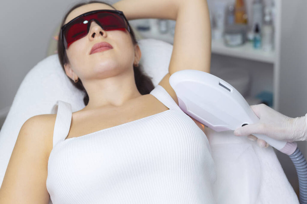 laser ontharing van oksel in moderne kosmetologie kliniek, volwassen vrouw doet epilatie in schoonheidssalon.  - Foto, afbeelding