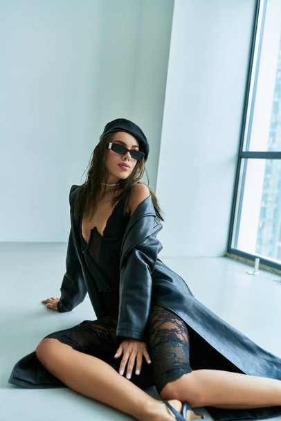 sexy outfit, beautiful woman in beret, sunglasses, lace underwear and leather coat sitting on floor - Photo, Image