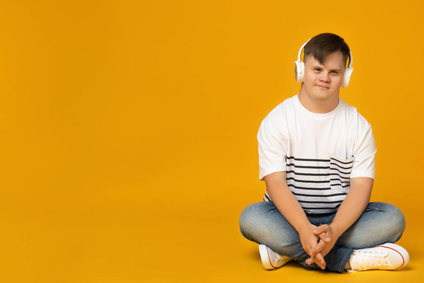 Lächelnder junger Mann mit Down-Syndrom in Brille, Musik über Kopfhörer hörend, Platz für Text - Foto, Bild