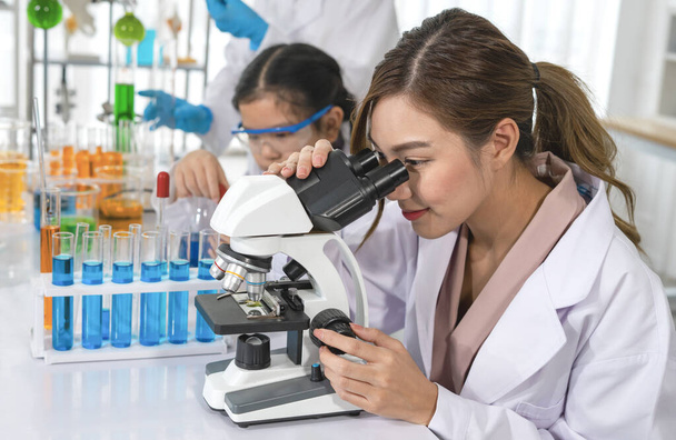 portret jonge aantrekkelijke vrouwelijke wetenschapper kijken in de microscoop, terwijl het onderwijs van de studenten in laboratoriumwetenschappen mentor clas - Foto, afbeelding