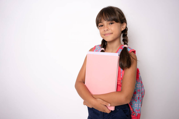 Mosolygó aktív kiváló tanuló iskolás lány gazdaság könyvek és másolókönyvek megy az iskolába visel táska elszigetelt fehér háttér - Fotó, kép