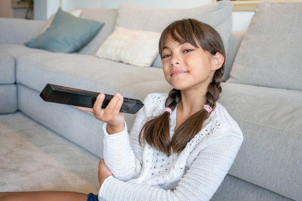 9-jähriges Kind sieht Fernsehen, wie es sich allein zu Hause auf einen weißen Teppich legt - Foto, Bild