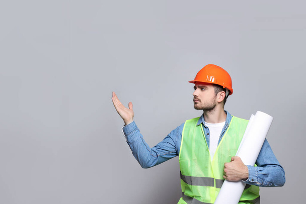 Ingenieur im Helm mit Zeichenpapier in der Hand auf grauem Hintergrund, Platz für Text - Foto, Bild