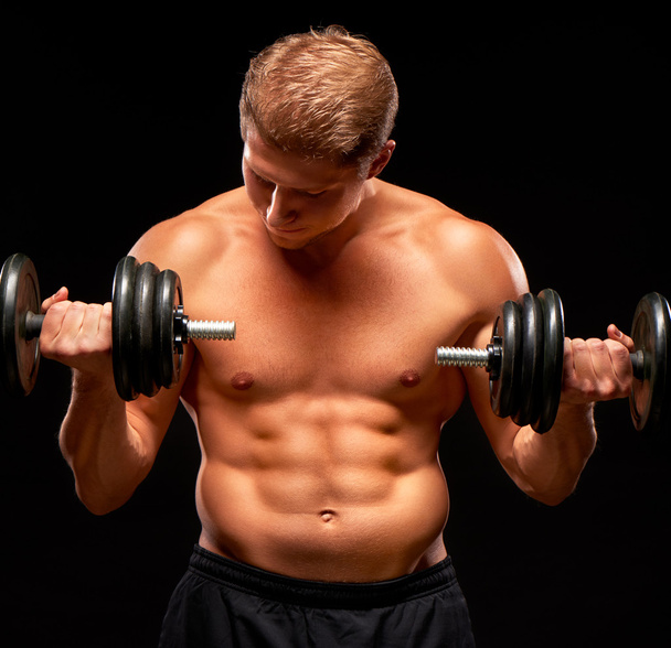 Powerful sportsman doing exercises for biceps with dumbbells on black - Fotó, kép