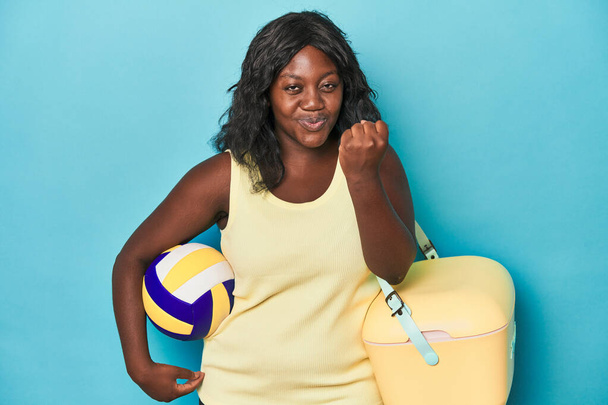 Young curvy woman with cooler and ball showing fist to camera, aggressive facial expression. - Photo, Image