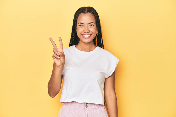 Giovane donna indonesiana su sfondo giallo studio gioioso e spensierato mostrando un simbolo di pace con le dita. - Foto, immagini