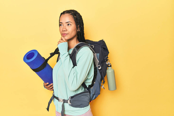 Indonesian woman ready for mountain trip on yellow looking sideways with doubtful and skeptical expression. - Photo, Image