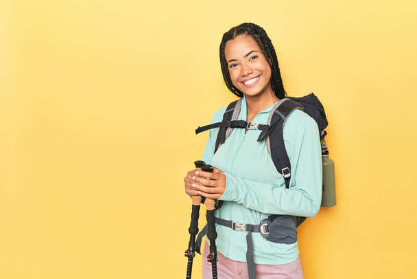 Indonesian woman with hiking gear on yellow happy, smiling and cheerful. - Photo, Image