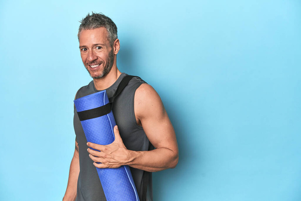 Sportler mit Fitnessmatte auf blauem Studiohintergrund - Foto, Bild