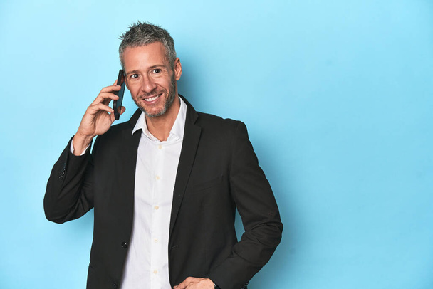 Бизнесмен в костюме разговаривает по телефону, на фоне синей студии - Фото, изображение