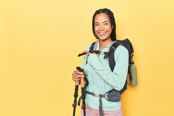 Mujer indonesia con equipo de senderismo en amarillo sonriendo y señalando a un lado, mostrando algo en espacio en blanco. - Foto, imagen