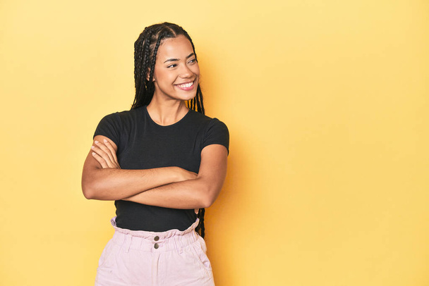 Young Indonesian woman on yellow studio backdrop smiling confident with crossed arms. - Fotó, kép
