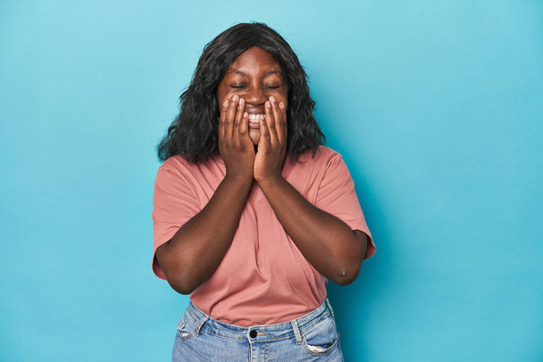 Νεαρή Αφροαμερικανή καμπυλωτή γυναίκα να γελάει για κάτι, να καλύπτει το στόμα με τα χέρια. - Φωτογραφία, εικόνα