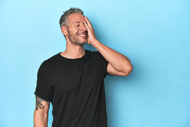 Middle-aged caucasian man on blue backdrop laughing happy, carefree, natural emotion. - Photo, Image