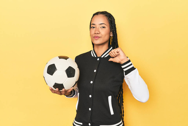 Индонезийская школьница с футбольным мячом на желтом чувствует себя гордой и уверенной в себе, пример для подражания. - Фото, изображение