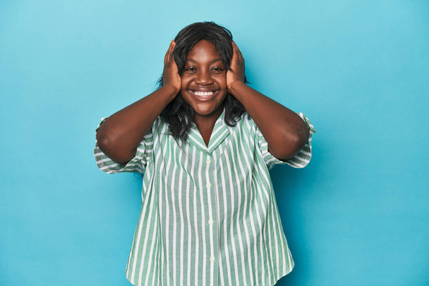 Νεαρή Αφροαμερικανή καμπυλωτή γυναίκα γελάει με χαρά κρατώντας τα χέρια στο κεφάλι. Έννοια ευτυχίας. - Φωτογραφία, εικόνα