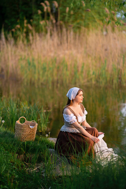Jolie jeune blanchisseuse en costume médiéval debout près de la rivière. Œuvre d'art conte de fées. - Photo, image