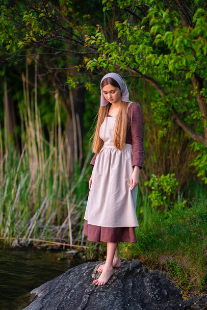 Hübsche junge Wäscherin in mittelalterlichem Kostüm steht am Fluss. Märchenhafte Kunstwerke. - Foto, Bild