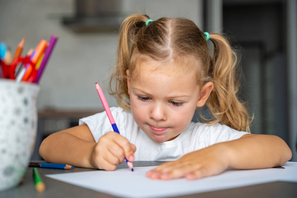 klein meisje tekent met gekleurde potloden in huis. Hoge kwaliteit foto.  - Foto, afbeelding