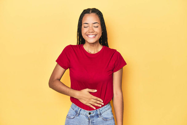 Young Indonesian woman on yellow studio backdrop touches tummy, smiles gently, eating and satisfaction concept. - Photo, Image