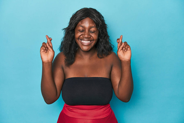 Young african american curvy woman crossing fingers for having luck - 写真・画像