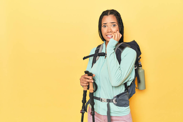 Indonesian woman with hiking gear on yellow biting fingernails, nervous and very anxious. - Photo, Image