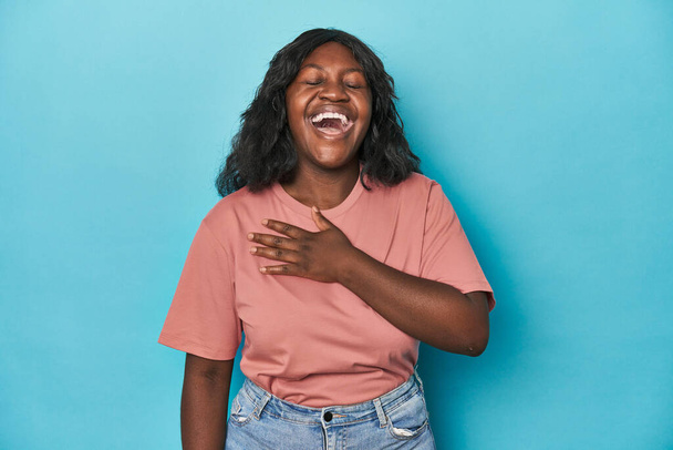 Νεαρή Αφροαμερικανή καμπυλωτή γυναίκα γελάει δυνατά κρατώντας το χέρι στο στήθος. - Φωτογραφία, εικόνα