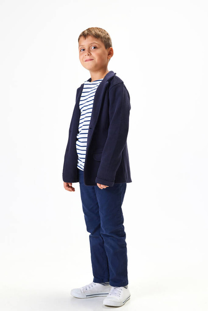 Smiling boy, child wearing blue uniform, smart casual clothes, standing against white studio background. Concept of childhood, school, education, fashion, style. Copy space for ad - Foto, Imagem